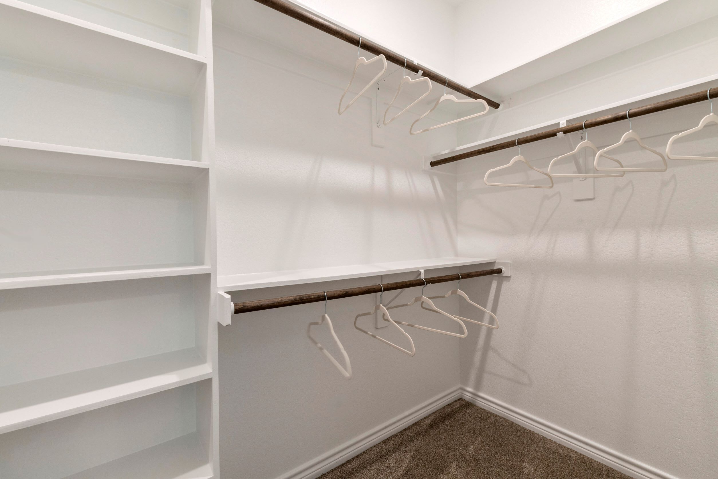 A walk-in closet with white shelves and wooden rods for hanging clothes.