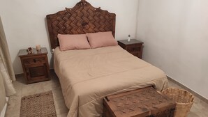A neatly arranged bedroom with a wooden headboard, a beige bedspread, two nightstands, a small bedside table, a woven basket, and a woven rug. - Resting house with pool! near the Media Luna Spring (Ciudad Fernández)