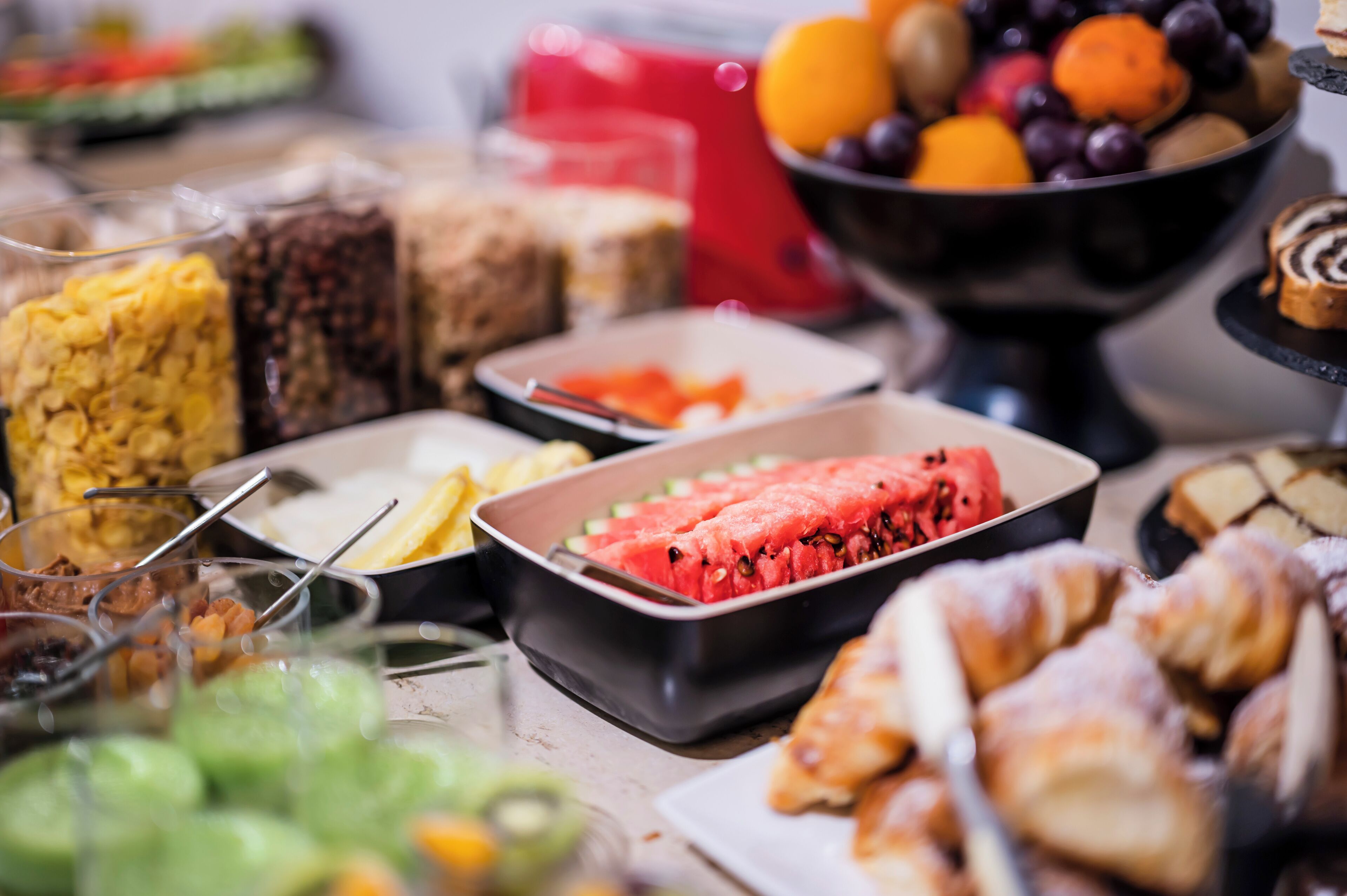 A buffet with various food items including fruits, pastries, and cereals.