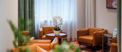 Habitación de hotel con un sofá de cuero marrón, una mesa redonda de madera con una planta en maceta y una alfombra estampada.