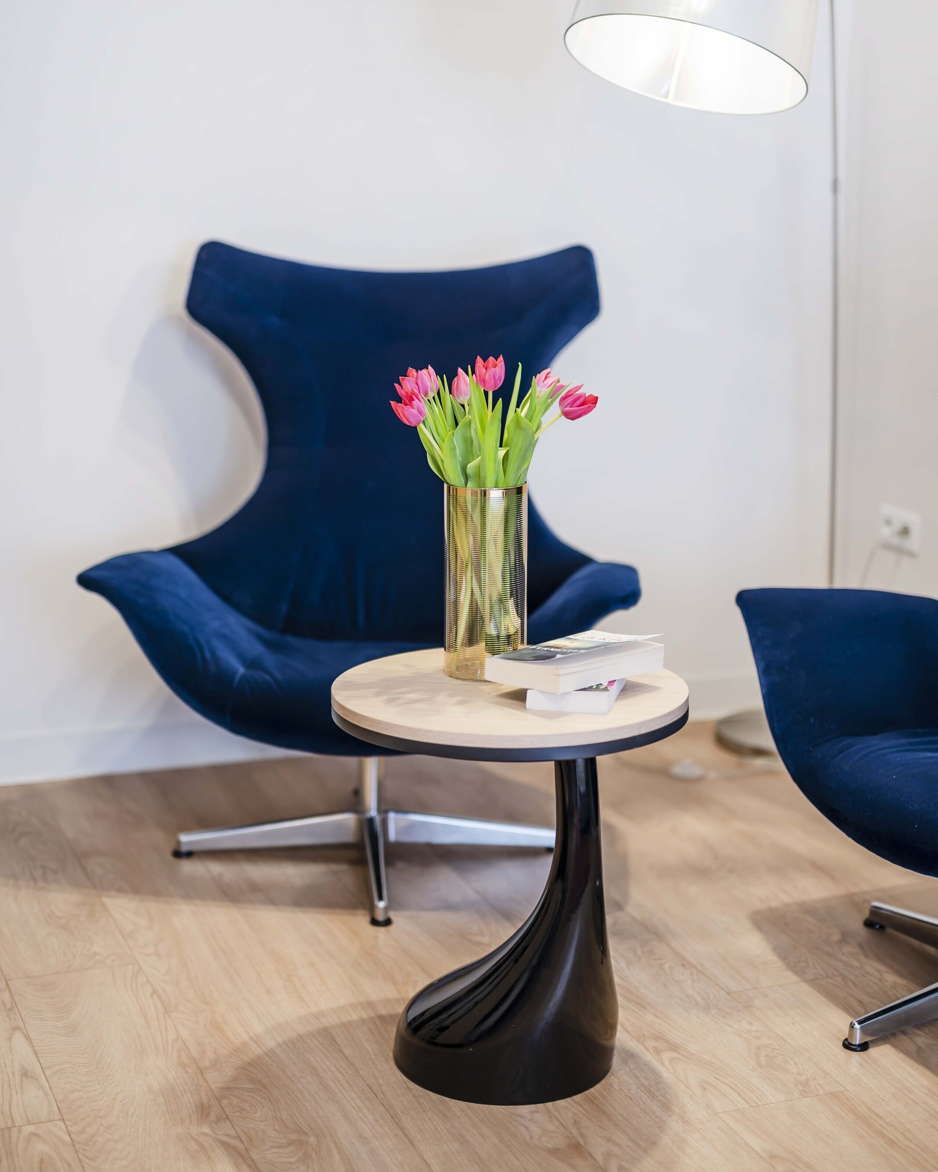 A modern room with a round table, a blue chair, and a vase with flowers.
