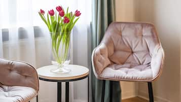 Una habitación con cama, dos sillas, una mesita con un florero y una ventana con cortinas.