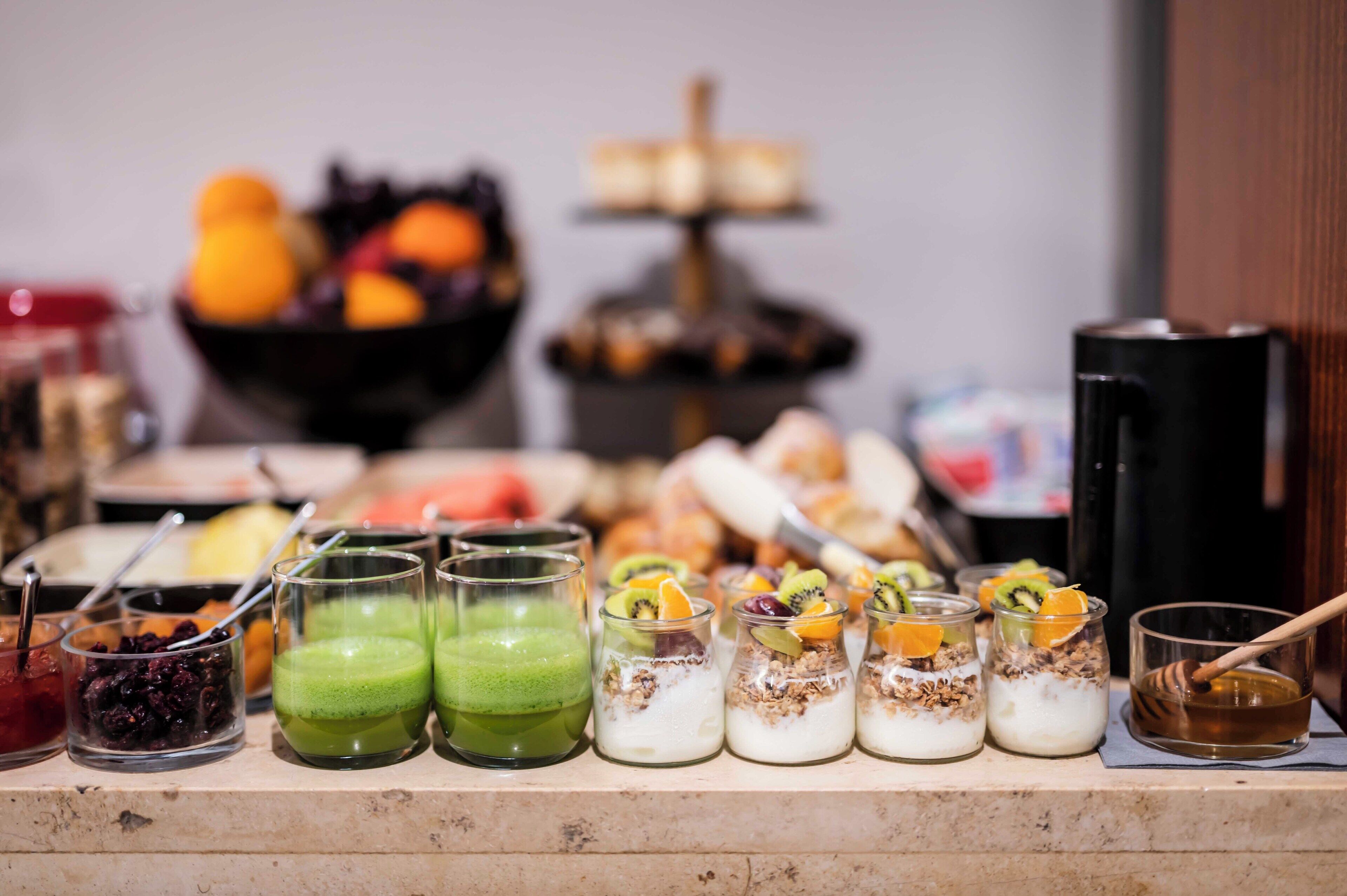 A buffet table with various food items and beverages, including fruit, granola, and smoothies.