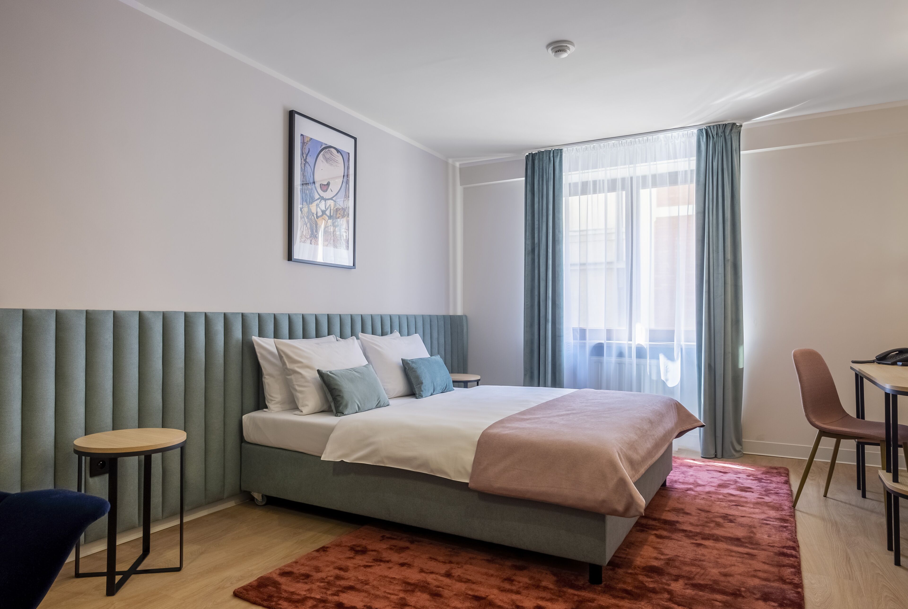 A modern bedroom with a bed, a small table, a chair, and a window with curtains.