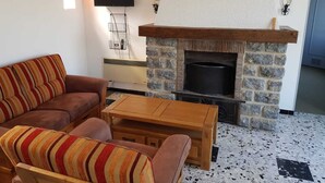 A living room with a stone fireplace, a brown sofa, a wooden coffee table, and a TV mounted on the wall. - house in the countryside in the heart of Bazois with terrace (50m2) and pleasure garden (Châtillon-en-Bazois)