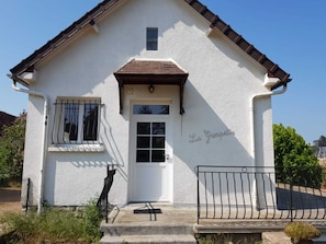 A white building with a brown roof, a white door, and a small window with bars.