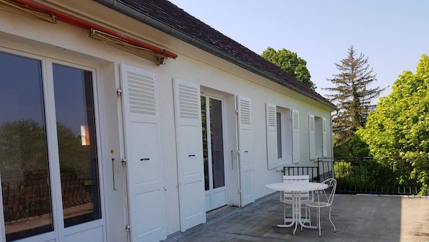 A building with white doors and shutters, a concrete patio, and a round table with chairs. - house in the countryside in the heart of Bazois with terrace (50m2) and pleasure garden (Châtillon-en-Bazois)