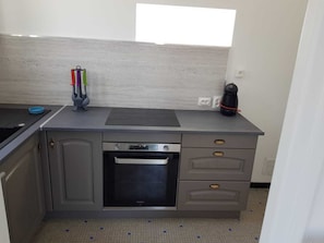 A compact kitchen with a built-in oven, a coffee maker, and a window above the countertop.
