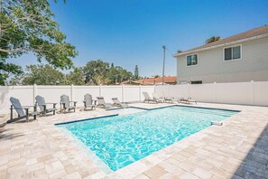 Una piscina rectangular con borde de baldosas, rodeada de sillones de descanso y una valla blanca.