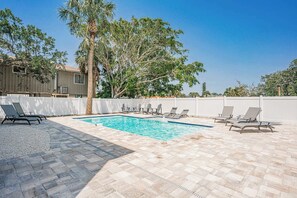 Une piscine rectangulaire entourée d’une clôture blanche, avec des chaises longues et un palmier.