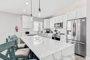 Une cuisine moderne avec des meubles blancs, un grand îlot central, des appareils en acier inoxydable et un extincteur.