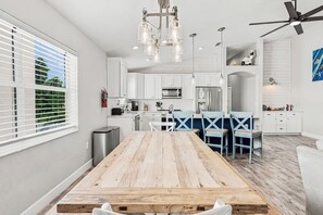 Eine moderne Küche mit weißen Schränken, einem Holztisch und einem Deckenventilator.