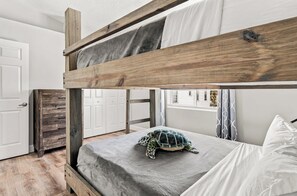 A bunk bed with a turtle on the lower bunk, a wooden dresser, and a window with curtains.