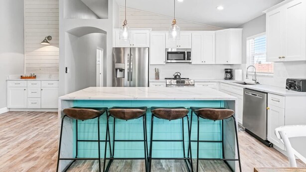 A modern kitchen with white cabinets, stainless steel appliances, a large island with bar stools, and pendant lighting. - Dolphin Dreamer-Golf Cart, Pool, BEACH! (Indian Rocks Beach)
