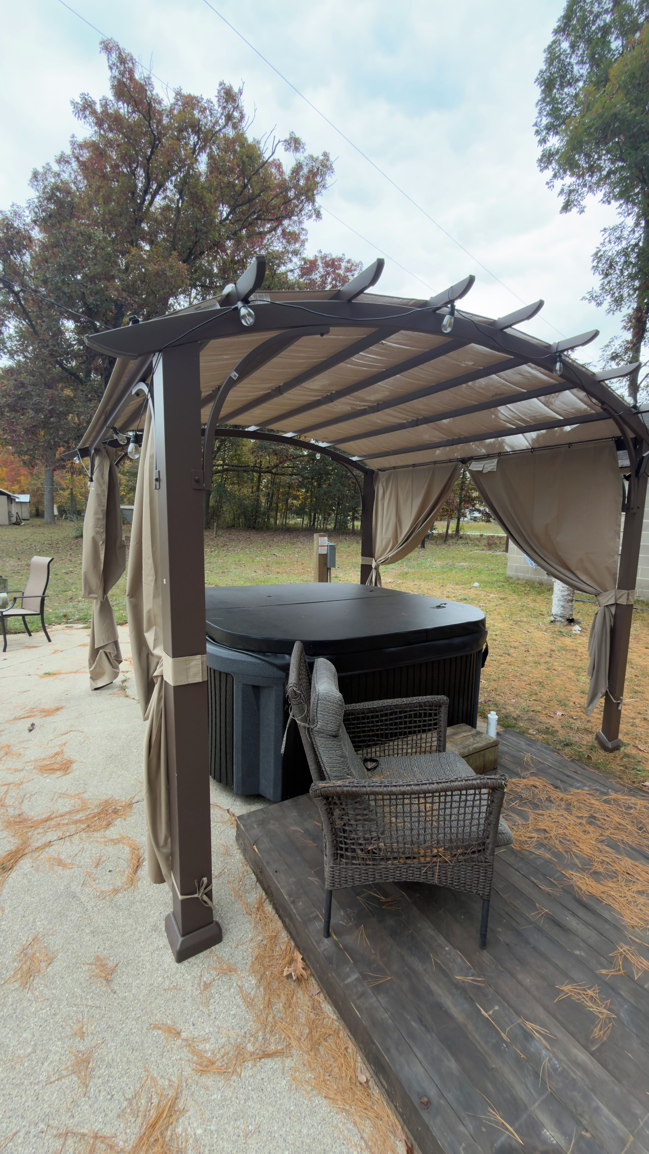 Un espacio de estar al aire libre techado con un jacuzzi, una silla y una estructura de pérgola.