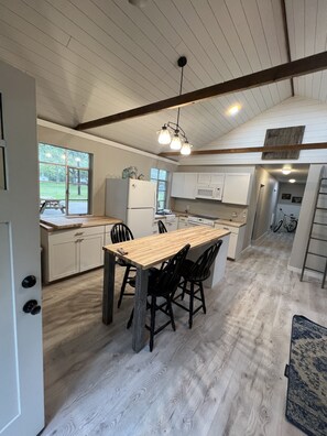 A spacious kitchen with a large island, white cabinetry, and a wooden floor. - Grays Riverside Camp Cabin 1. (Big Rapids)