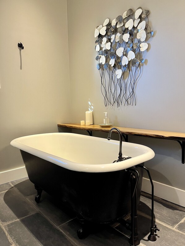 Ein Badezimmer mit einer freistehenden Badewanne, einem Holzbadezimmer-Möbelkorpus und einem an der Wand befestigten dekorativen Metallkunstwerk.