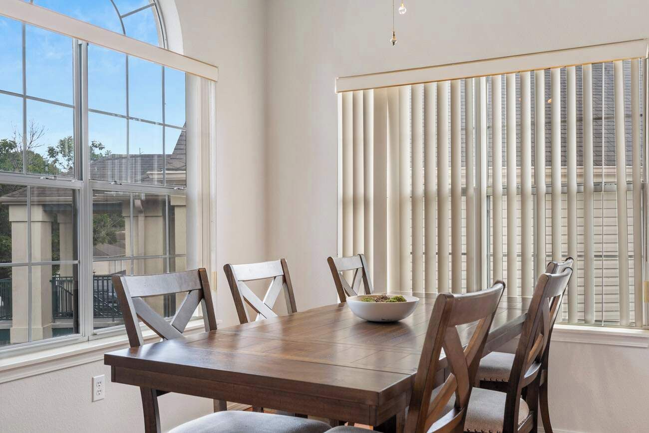 A dining area with a wooden table and chairs, a bowl of food, and a window with blinds.