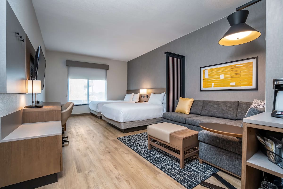 Ein modernes Hotelzimmer mit Bett, Sofa, Schreibtisch und einem großen Fenster.
