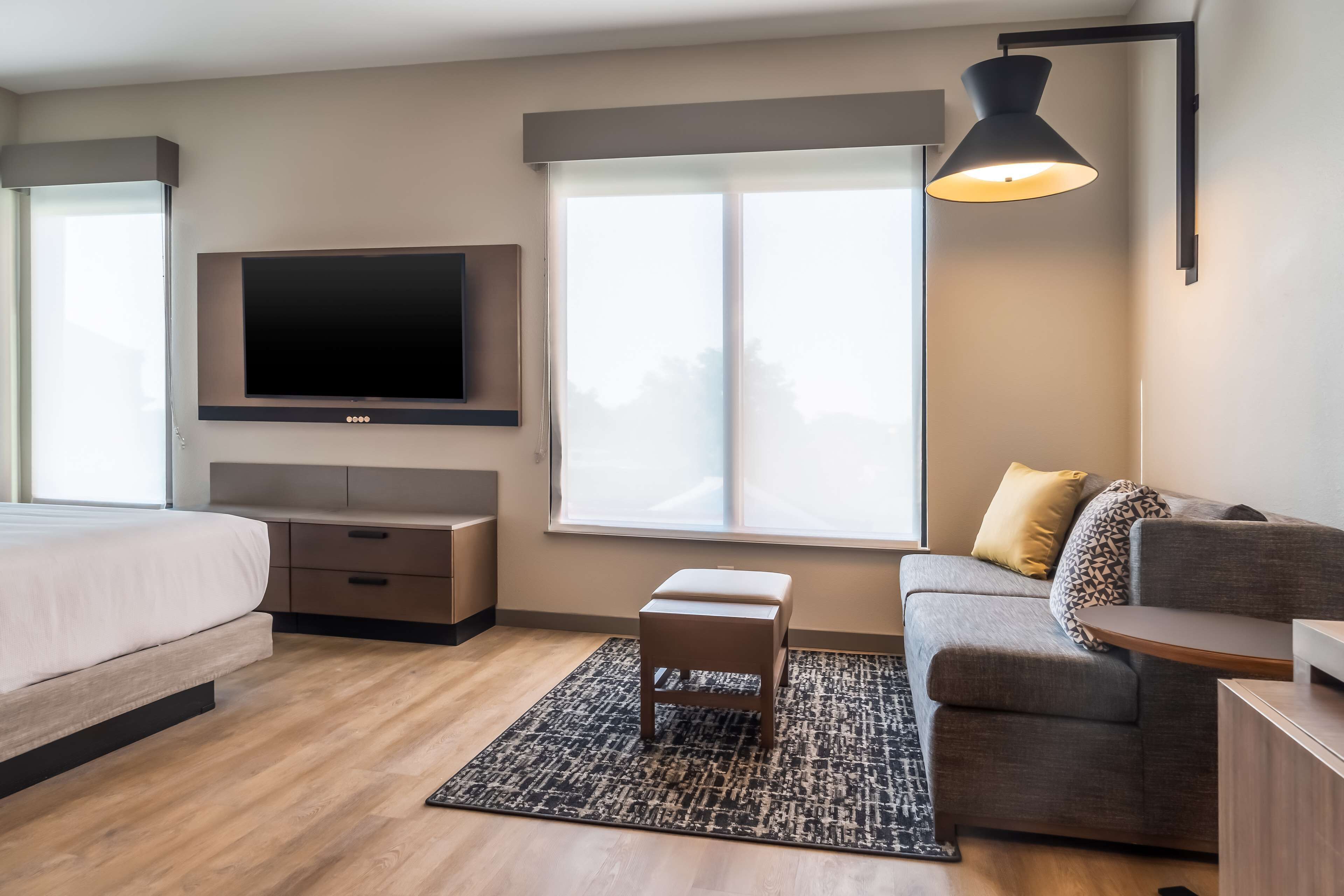 Une chambre d’hôtel moderne équipée d’un lit, d’un canapé, d’un téléviseur fixé au mur et d’une grande fenêtre.