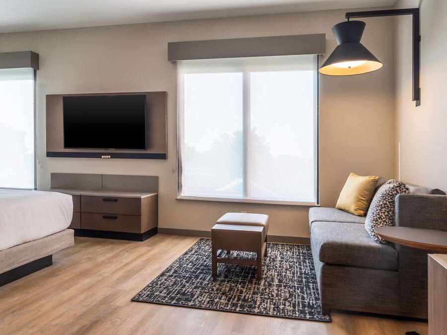 Una habitación de hotel moderna con cama, sofá, televisor montado en la pared y un gran ventanal.