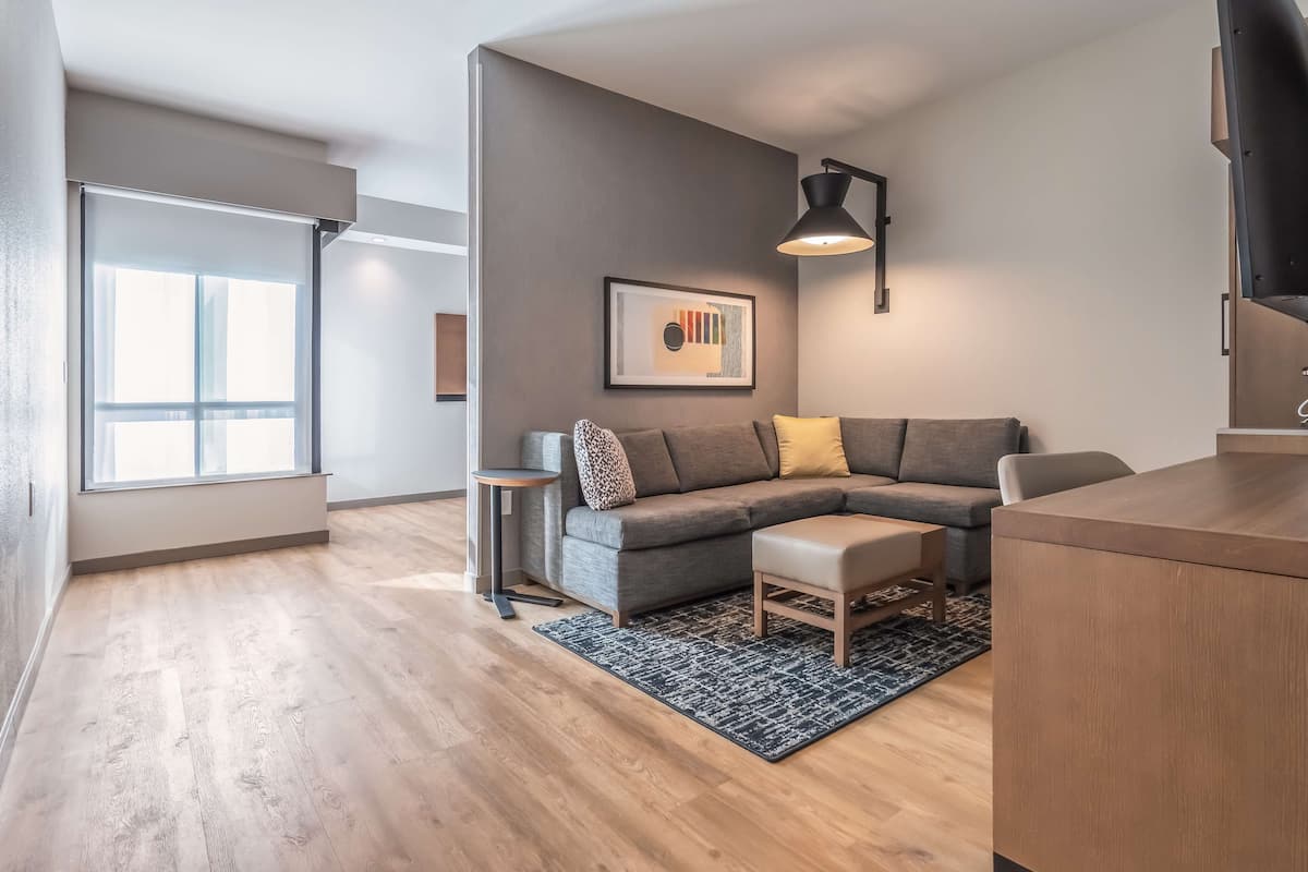 Ein modernes Wohnzimmer mit einem grauen Ecksofa, einem kleinen Beistelltisch und einem Couchtisch aus Holz.