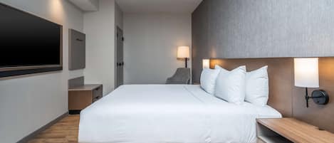 A modern hotel room with a large bed, a flat-screen TV, a bedside table, and a wall-mounted lamp.