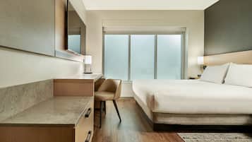 Quarto de hotel moderno com uma cama grande, uma escrivaninha e uma cadeira. Há uma janela ampla com vista para a cidade.