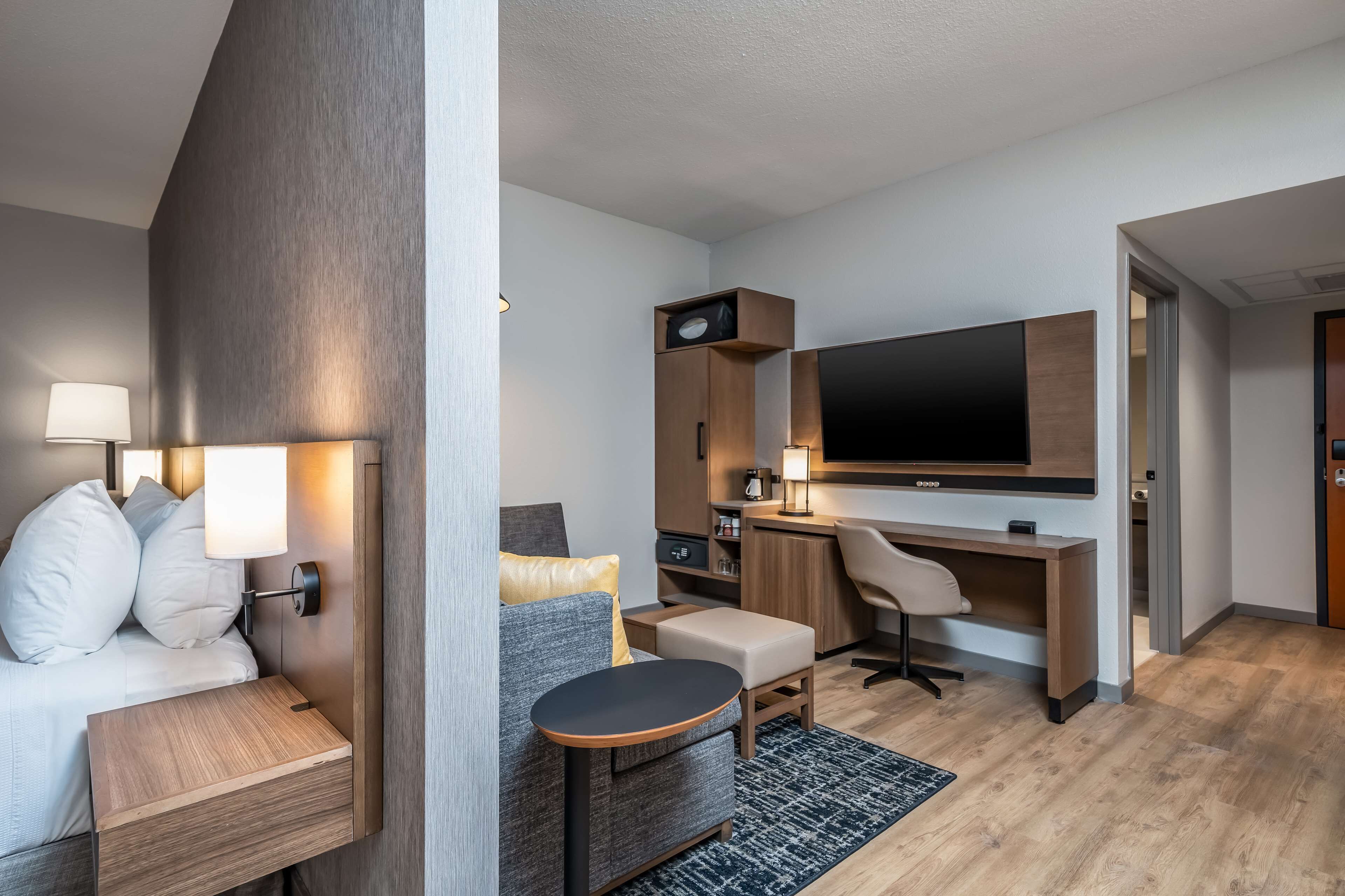 Una habitación de hotel moderna con una cama, un escritorio, una silla, un televisor y una mesita.