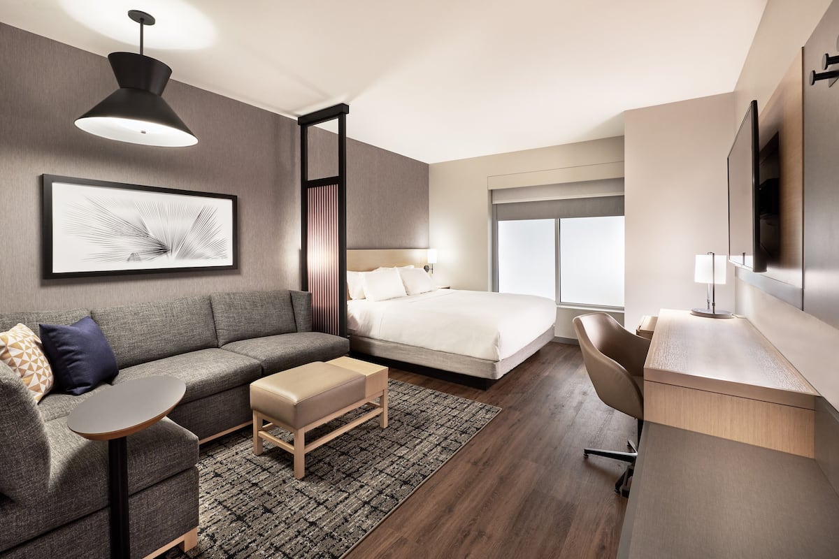 Ein modernes Hotelzimmer mit einem großen Bett, einer Couch, einem Schreibtisch und einem Fernseher.