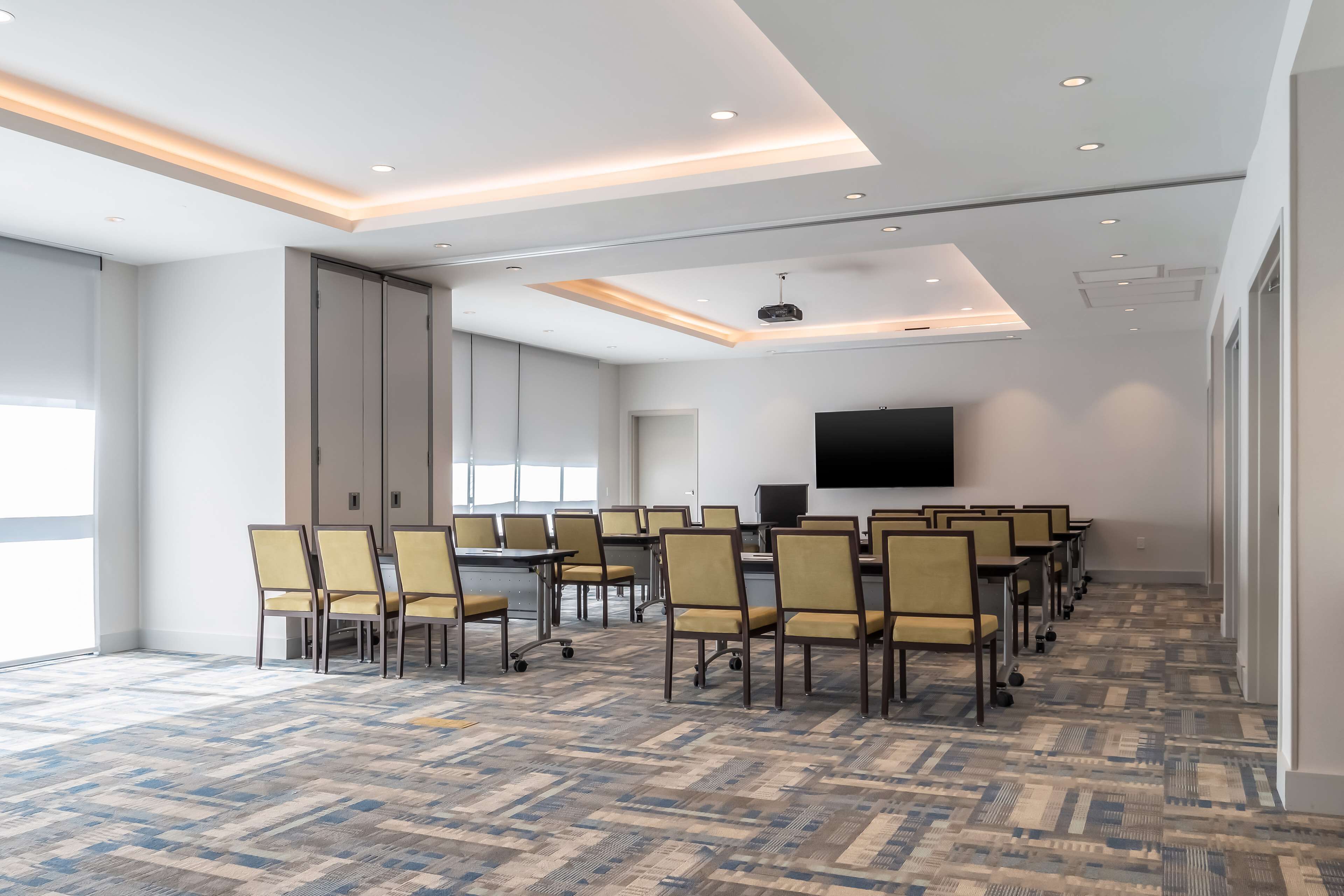 Un salón de conferencias con filas de sillas, un televisor de pantalla plana grande y una alfombra estampada.