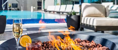 Ein Poolbereich mit Feuerstelle, Liegestühlen und einem Glas Wein.