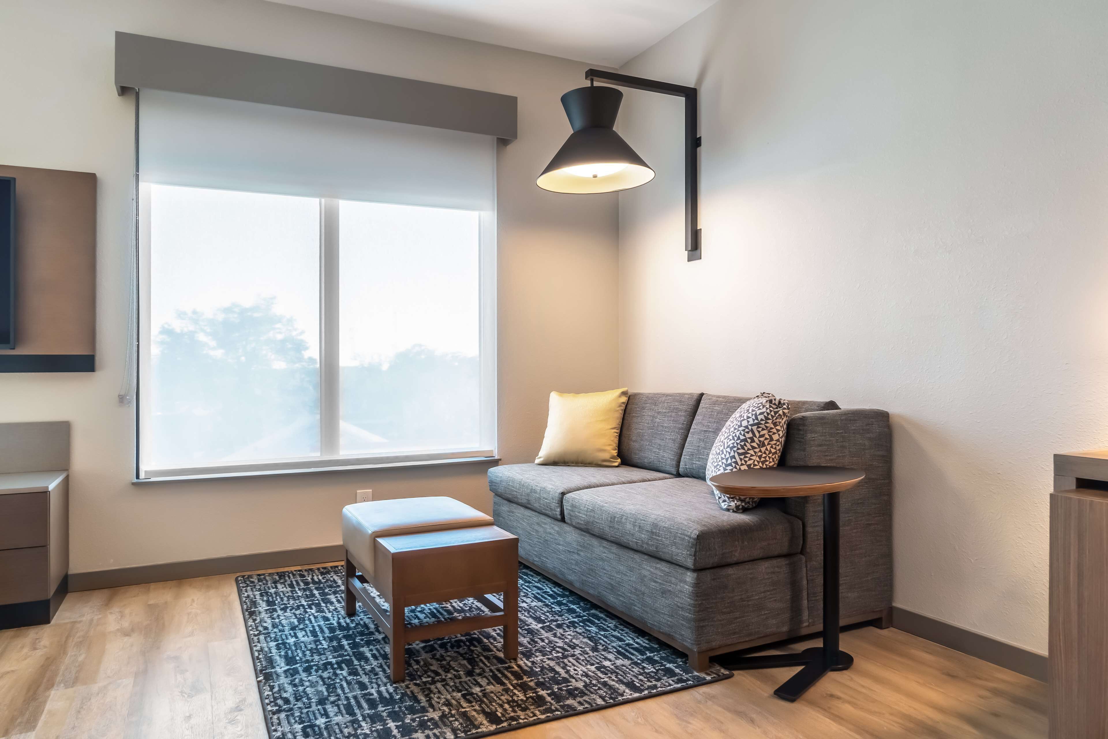 Una sala de estar moderna con un sofá gris, un pequeño banco de madera, una mesa redonda y una lámpara de pie negra.