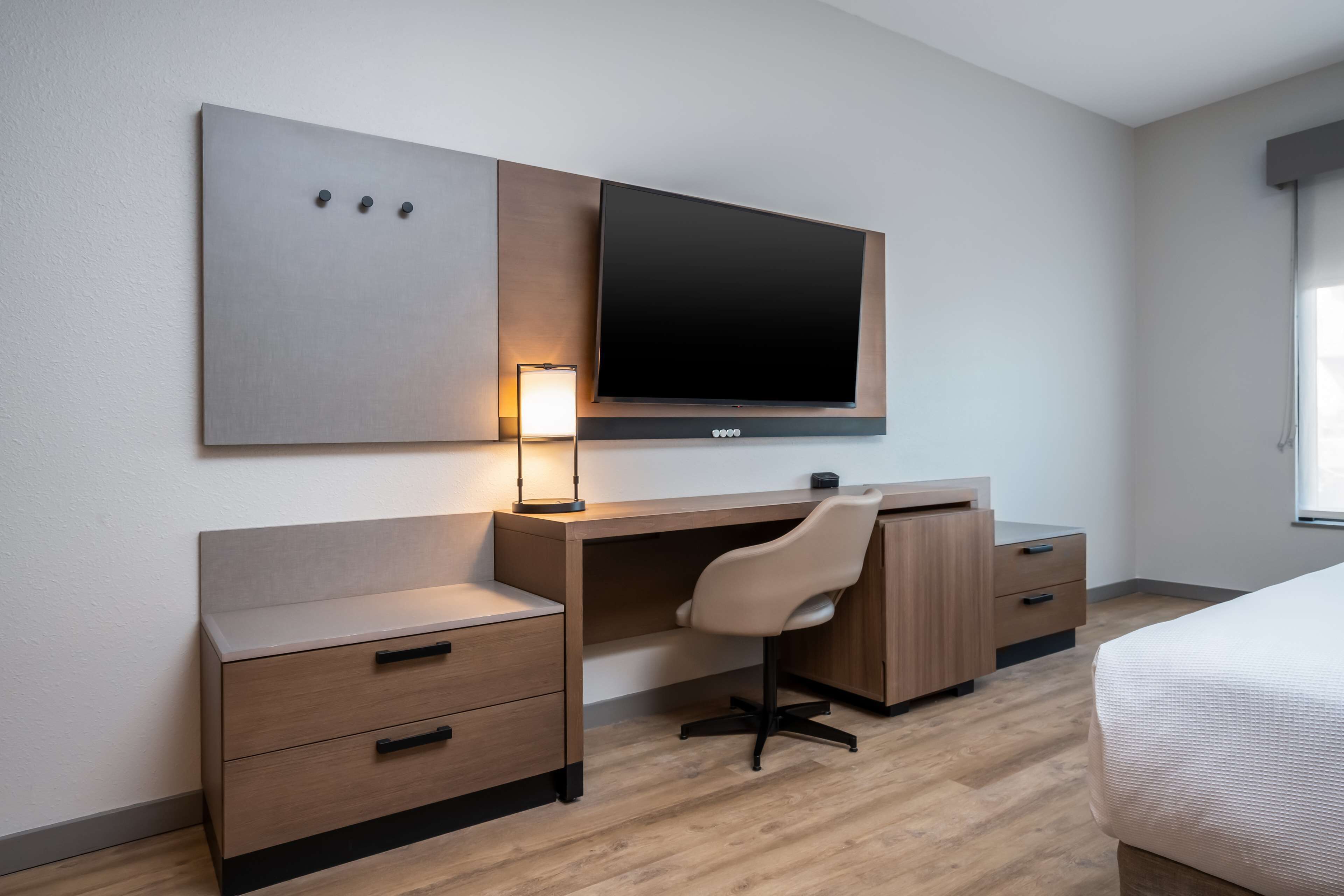 Habitación de hotel con escritorio de madera, una silla, televisor montado en la pared, mesita de noche y cama.