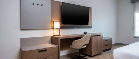 Habitación de hotel con escritorio de madera, una silla, televisor montado en la pared, mesita de noche y cama.
