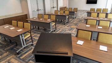 A conference room with multiple tables and chairs, a flat-screen TV on the wall, and a carpeted floor.
