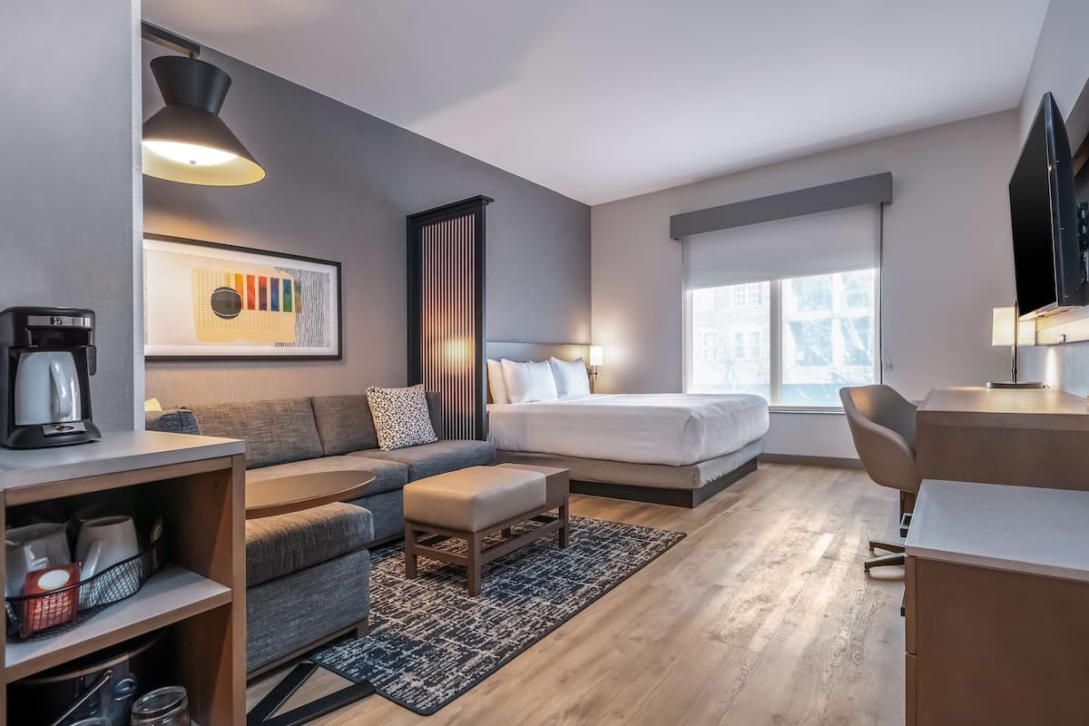 Ein modernes Hotelzimmer mit Sofa, Bett, Schreibtisch und Kaffeemaschine.