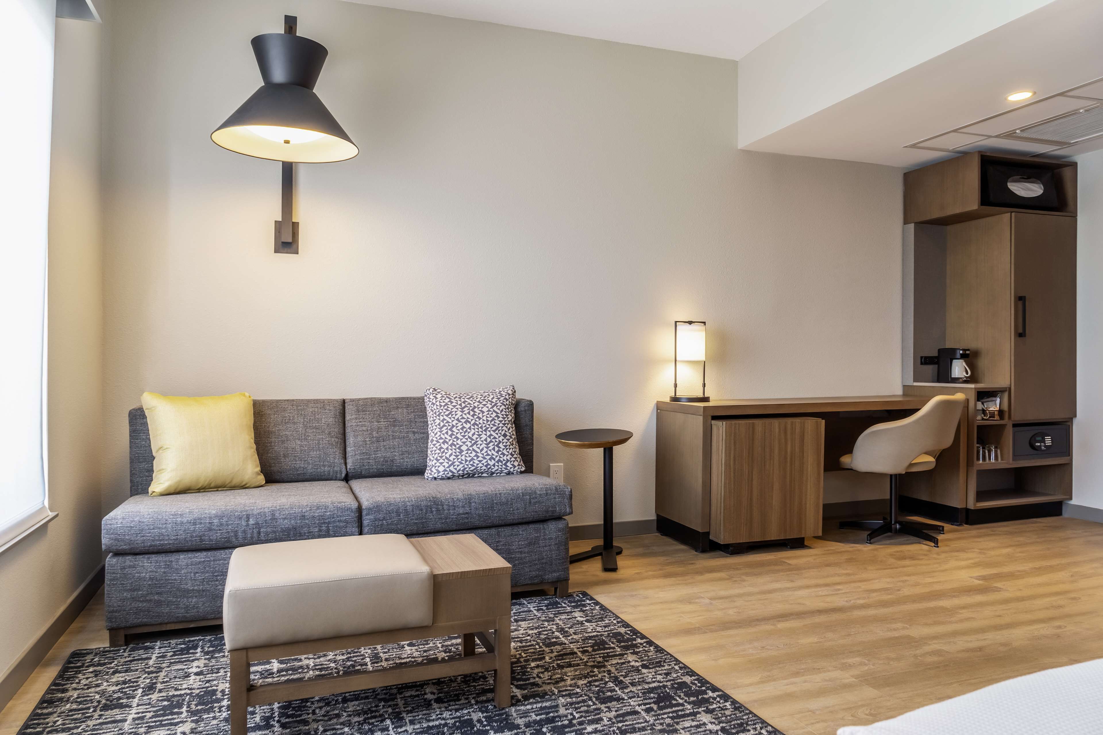 Una sala de estar moderna con un sofá gris, una mesita, un tapete estampado y un escritorio de madera con una silla.