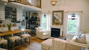 A spacious living room with a fireplace, a dining area with wooden furniture, and a kitchen with white cabinets and a wooden floor.