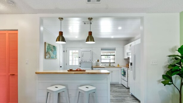Een moderne keuken met een centraal eiland, barstoelen, hanglampen en uitzicht op de eethoek.