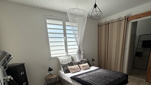 A bedroom with a bed, a standing lamp, a camera on a tripod, and a window with curtains. - Le Loft - Villa Ansalane (Les Trois-Îlets)