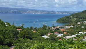 A coastal town with houses, a marina, and a view of the sea and distant mountains. - Le Loft - Villa Ansalane (Les Trois-Îlets)