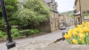 A stone bench with a metal railing, a street with buildings, and a car parked on the road. - 1 Chews Cottage (Harrogate)