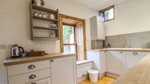 A modern kitchen with white cabinets, a wooden countertop, and a window providing natural light. - 1 Chews Cottage (Harrogate)