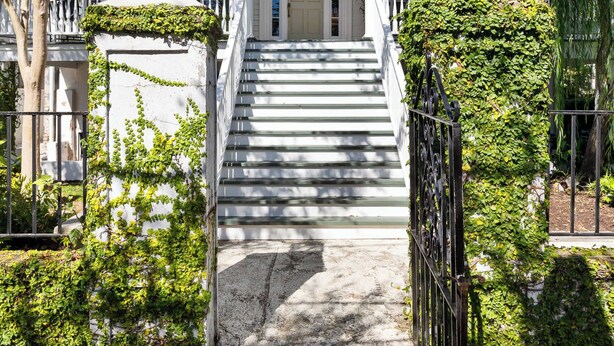 A white colonial-style house with a front porch, steps, and a gated entrance.