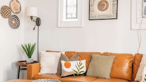 Una sala de estar moderna con un sofá de cuero, almohadones decorativos, una lámpara de pie y obras de arte en la pared.