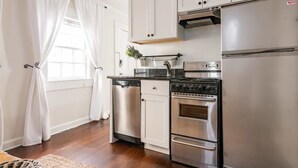 Cocina con armarios blancos, un refrigerador de acero inoxidable, estufa y lavavajillas.