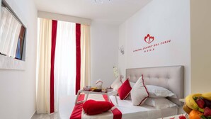 A hotel room with a bed, a bedside table with fruit, and a wall with a logo. - Ripetta Luxury Del Corso (Rome)