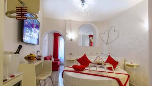 A modern bedroom with a round bed, red accents, a TV, and a unique chandelier. - Ripetta Luxury Del Corso (Rome)