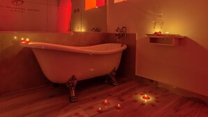 A bathroom with a freestanding bathtub, a mirror, a shelf with candles, and a wall with a heart-shaped design. - Ripetta Luxury Del Corso (Rome)